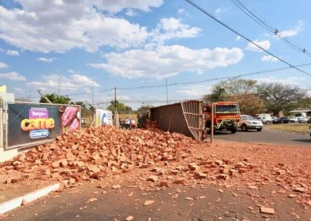 Caminhão com tijolos tomba em rotatória e motorista fica preso às ferragens
